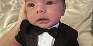 Cole is registered to the contest to win money with this photo: baby, infant, tuxedo, bow_tie, clothing, portrait, hand, bed, blanket, cute, face, eyes, skin, newborn, person, indoors, soft, expression, small, child