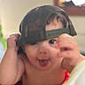 Zion is registered to the contest to win money with this photo: baby, child, infant, portrait, face, smiling, happy, indoor, hat, clothing, hands, fists, close_up, looking_at_camera, playful, sitting, home, window, soft_focus, photograph