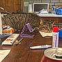 cat, tabby_cat, table, clutter, napkin, snacks, pen, phone_stand, tube, can, wooden_table, indoor, resting, sleepy, furniture, kitchen, background, container, door, plastic_bottle