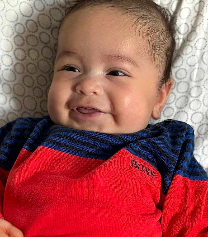 Islem a rejoint le concours — aidez-le/la à gagner de superbes lots ! baby, infant, smile, smiling, face, cheeks, eyes, hair, portrait, close_up, sweater, striped_sweater, red_clothing, blue_clothing, brand_logo, bedding, patterned_sheet, lying_down, cute, happy