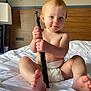 Astella joined the competition — help win amazing prizes! baby, child, diaper, bed, white_bedspread, holding, black_object, blue_eyes, smiling, sitting, bare_chest, feet, hotel_room, wooden_headboard, lamp, curious, soft_light, indoors, cute, portrait