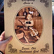 Madison is registered to the contest to win money with this photo: child, toddler, girl, vintage, old_fashioned, clothing, wood, bottle, smile, portrait, decorative_text, sepia, hand, photo_board, rustic, bow, sitting, holding, background, person