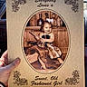 child, toddler, girl, vintage, old_fashioned, clothing, wood, bottle, smile, portrait, decorative_text, sepia, hand, photo_board, rustic, bow, sitting, holding, background, person