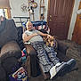 man, dog, recliner, living_room, casual_clothing, plaid_pants, slippers, carpet, door, lamp, wall_art, stuffed_animal, balloon, magazine_bag, relaxation, pet, home_interior, smiling, seated, cozy