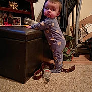 Killian is registered to the contest to win money with this photo: child, baby, toddler, pajamas, bear_prints, standing, ottoman, carpet, bottle, living_room, furniture, jacket, coat_rack, photo_frame, family_photo, floor, belt, cardboard_box, shelf, candid