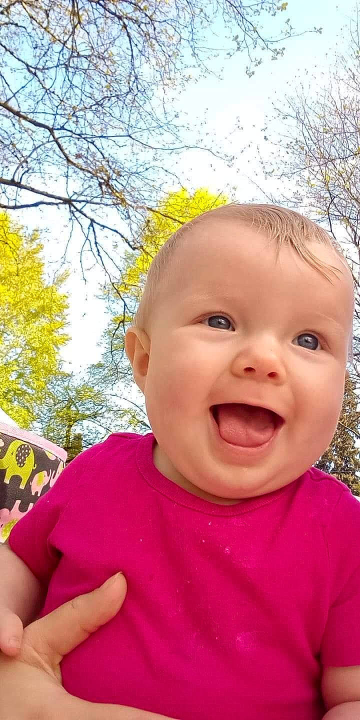 Phoebe is registered to the contest to win money with this photo: baby, cheek, chin, eye, face, facial_expression, gesture, grass, happy, head, lip, mouth, nose, people_in_nature, person, pink, plant, skin, sky, smile