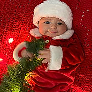 Sophie joined the competition — help win amazing prizes! baby, christmas, holiday, red, santa_hat, santa_suit, knitted_blanket, lights, greenery, festive, cute, infant, holiday_decor, smile, portrait, cozy, indoors, celebration, child, winter