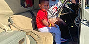 Jasper joined the competition — help win amazing prizes! child, children, vehicle, car, military_vehicle, reflection, red_shirt, gray_pants, sneakers, steering_wheel, seat, window, sunlight, outdoor, daytime, person, portrait, interior, casual_clothing, curious