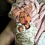 baby, infant, blanket, pink_bow, onesie, floral_pattern, hand, foot, person, skin, lap, couch, fabric, soft_texture, headband, cute, newborn, expression, indoors, relaxed