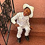child, boy, smiling, winking, white_suit, hat, stairs, carpet, black_shoes, railing, indoors, happy, formal_wear, portrait, person, fashion, cute, dressed_up, sitting, fun
