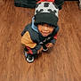Braxton joined the competition — help win amazing prizes! child, toddler, hat, pom_pom, smiling, crouching, wooden_floor, colorful_clothing, indoor, footwear, black_shoes, patterned_fabric, happy, face, person, winter_wear, playful, looking_up, floor, cute
