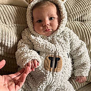 Judith participe au concours pour gagner de l'argent avec cette photo : baby, child, costume, sheep_costume, couch, hand, holding, finger, fuzzy_clothing, infant, cute, indoors, soft_texture, beige, seated, portrait, expression, cozy, warm, person