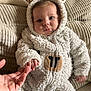 baby, child, costume, sheep_costume, couch, hand, holding, finger, fuzzy_clothing, infant, cute, indoors, soft_texture, beige, seated, portrait, expression, cozy, warm, person