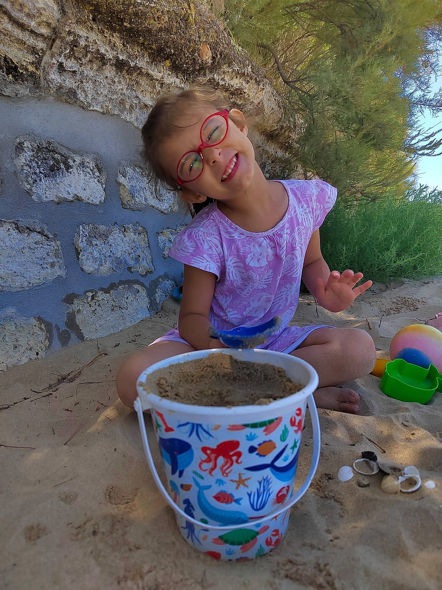 Léa participe au concours pour gagner de l'argent avec cette photo : bucket, child, cup, drinkware, earthenware, fun, happy, joy, leisure, person, play, pottery, recreation, sand, sitting, smile, soil, t_shirt, toddler, tree