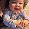baby, child, curly_hair, smiling, onesie, rainbow_pattern, indoor, holding_hand, happy, cute, portrait, infant, top_knot, person, young_child, playful, warm_lighting, closeup, seated, family