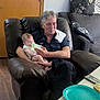Spring is registered to the contest to win money with this photo: man, baby, feeding, bottle, chair, leather_chair, couch, cushions, door, table, plate, floor, wood_floor, person, indoor, casual, comfort, home, care, family
