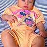 Elena is registered to the contest to win money with this photo: baby, child, infant, striped_bedspread, orange_clothing, minnie_mouse, cartoon_character, cute, portrait, laying_down, curly_hair, soft_lighting, indoors, relaxed, toddler, shorts, tshirt, barefoot, skin, expression