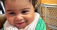 Marciano joined the competition — help win amazing prizes! baby, child, smiling, curly_hair, green_shirt, bib, indoor, baby_gate, wooden_door, happy, face, portrait, cute, infant, person, skin, sitting, closeup, young_child, playful