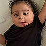 Marciano is registered to the contest to win money with this photo: baby, child, curly_hair, black_clothing, lying_down, white_background, infant, playful, face, portrait, raised_arm, indoors, closeup, expression, young_child, person, cute, head, skin, smiling