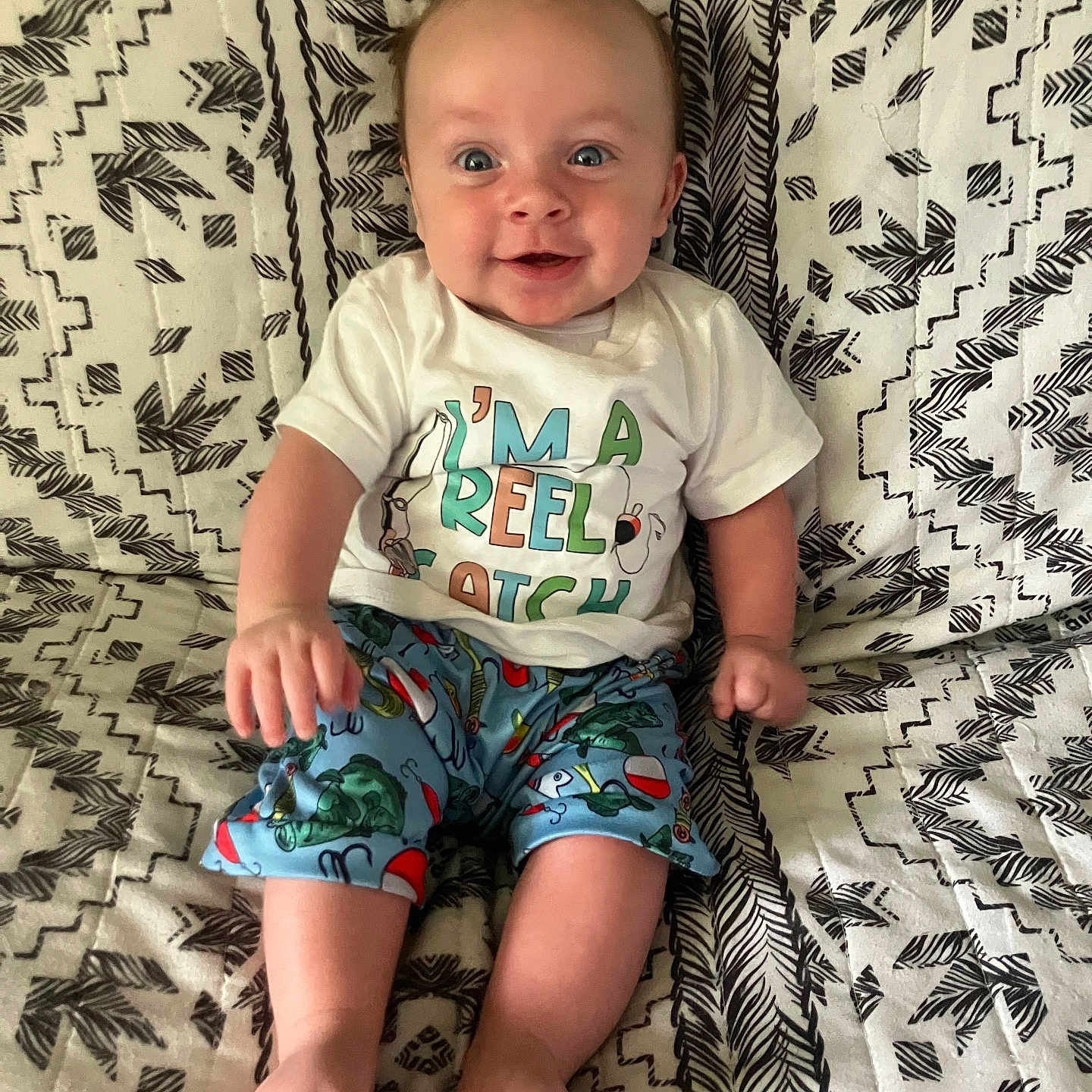 Daniel joined the competition — help win amazing prizes! baby, child, infant, smile, happy, clothing, shirt, shorts, patterned_blanket, sitting, feet, face, blue_shorts, white_shirt, cute, portrait, indoors, person, bright_eyes, joy