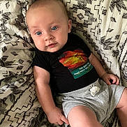 Daniel is registered to the contest to win money with this photo: baby, black_shirt, blanket, blue_eyes, child, closeup, colorful_graphic, cute, family_photo, gray_shorts, indoors, infant, looking_at_camera, lying_down, natural_light, patterned_fabric, portrait, relaxed, seated, wide_eyed