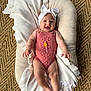 baby, infant, smiling, headband, bow, pink_romper, knitted, blanket, cushion, woven_rug, floor, happy, cute, milestone, celebration, child, portrait, indoor, person, laying