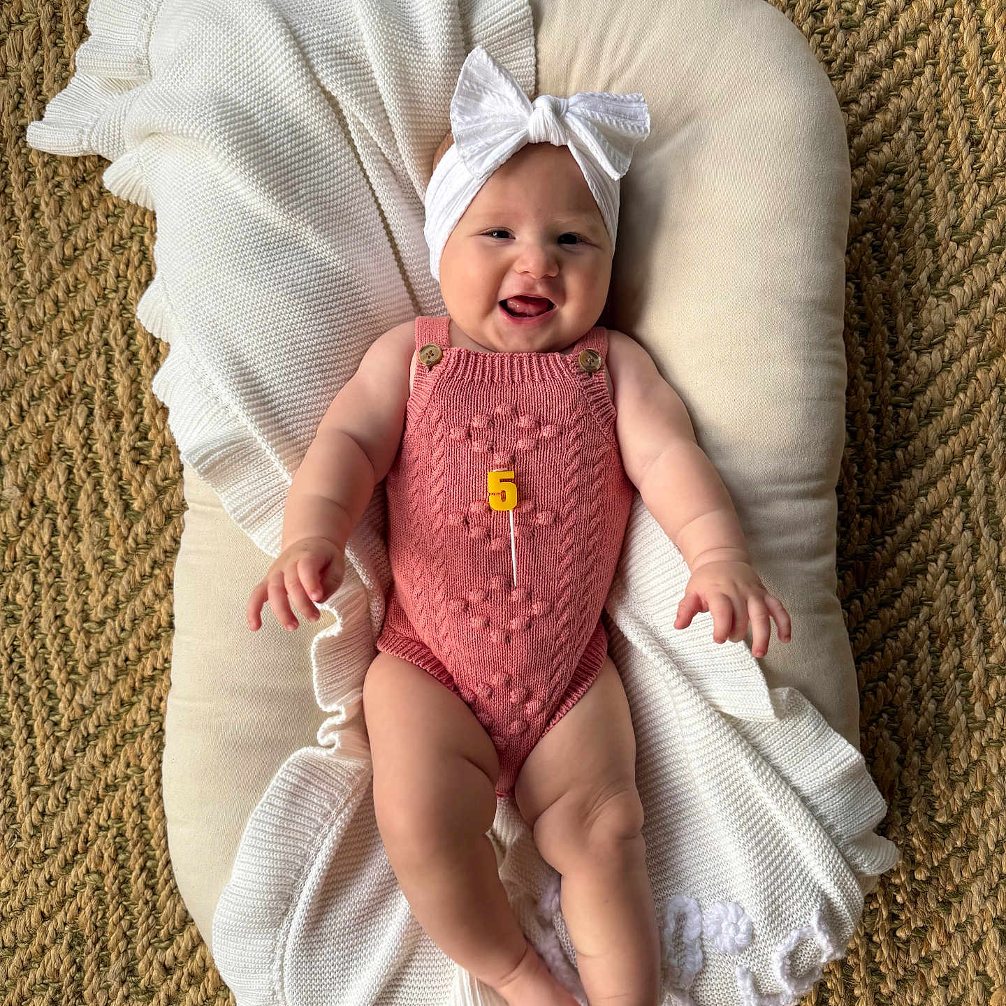 Lilia is registered to the contest to win money with this photo: baby, blanket, bow, celebration, child, cushion, cute, floor, happy, headband, indoor, infant, knitted, laying, milestone, person, pink_romper, portrait, smiling, woven_rug