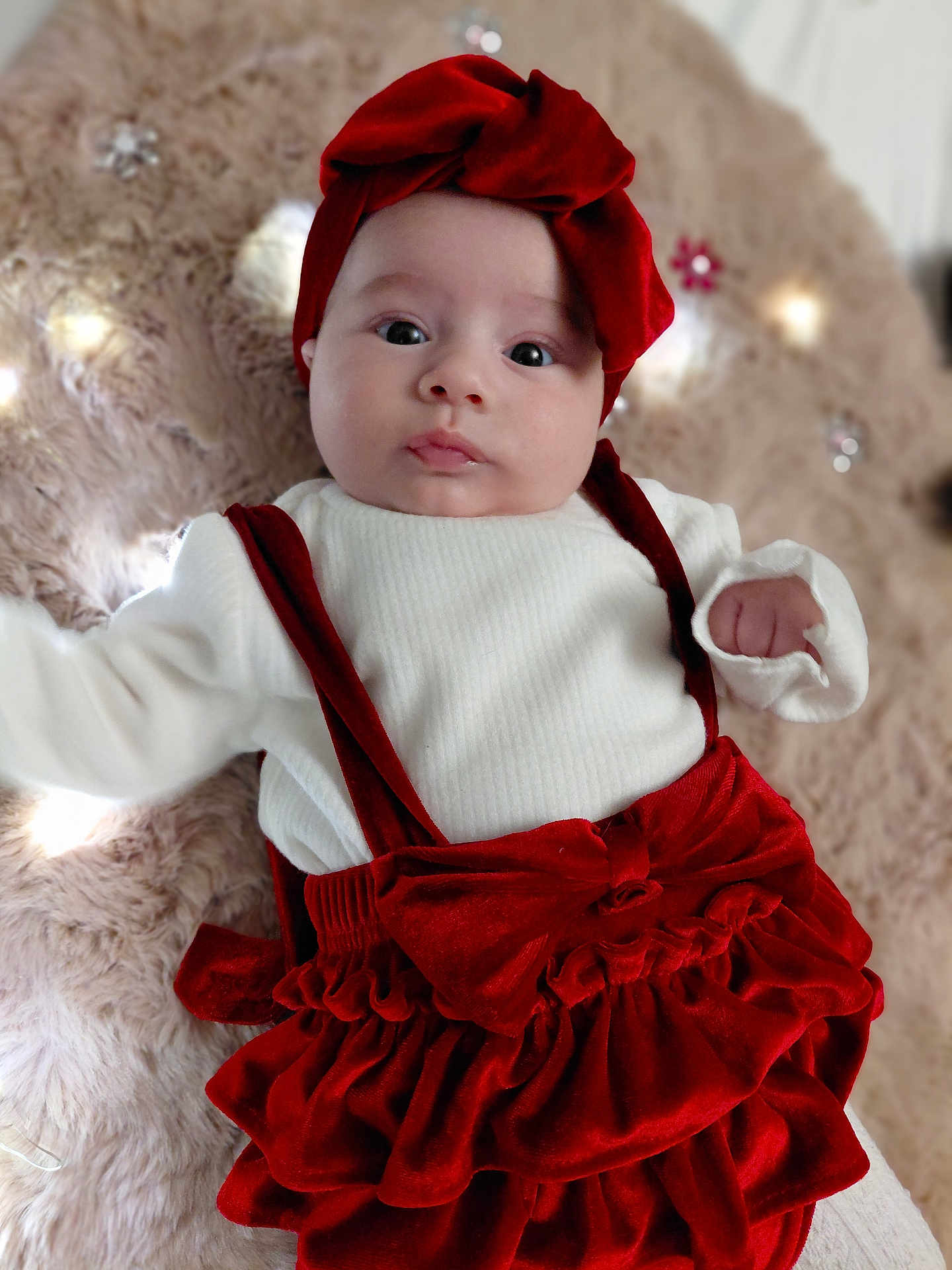 Lila a rejoint le concours — aidez-le/la à gagner de superbes lots ! baby, infant, red_bow, red_headband, white_shirt, velvet_clothing, plush_blanket, lights, flower_decor, cute, portrait, indoor, child, young_baby, face, looking_at_camera, soft_texture, cozy, holiday_outfit, adorable