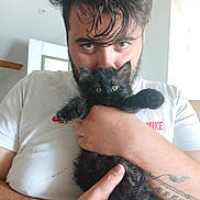 April a rejoint le concours — aidez-le/la à gagner de superbes lots ! man, kitten, black_cat, holding, tattoo, white_tshirt, indoor, portrait, cute, pet, animal, feline, face, eyes, hair, hand, cozy, closeup, expression, casual