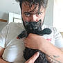 man, kitten, black_cat, holding, tattoo, white_tshirt, indoor, portrait, cute, pet, animal, feline, face, eyes, hair, hand, cozy, closeup, expression, casual