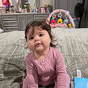 Valerie joined the competition — help win amazing prizes! baby, child, infant, pink_onesie, bed, toy, bedroom, dresser, curly_hair, sitting, cute, face, indoor, soft_lighting, childrens_toy, plaything, carpet, blanket, person, young_child
