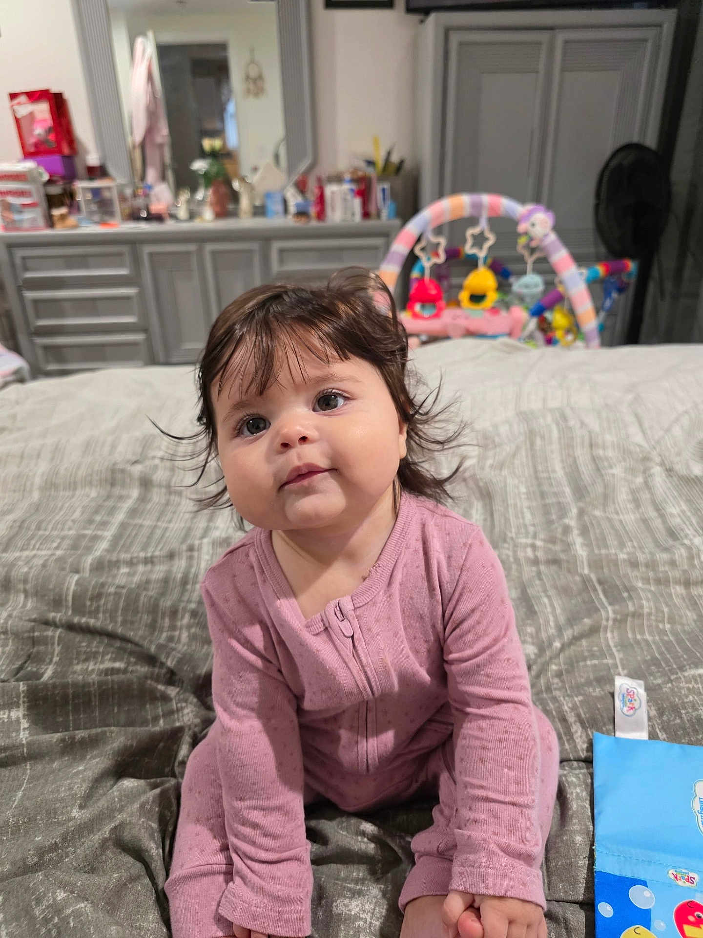 Valerie joined the competition — help win amazing prizes! baby, child, infant, pink_onesie, bed, toy, bedroom, dresser, curly_hair, sitting, cute, face, indoor, soft_lighting, childrens_toy, plaything, carpet, blanket, person, young_child