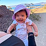 baby, child, smiling, hat, purple_hat, onesie, teddy_bear_pattern, outdoor, desert, lake, nature, sunny, person, holding, happy, face, portrait, arm, clothing, daytime