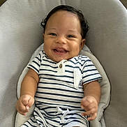 Levi is registered to the contest to win money with this photo: baby, child, smiling, striped_clothing, romper, curly_hair, seat, cushion, indoor, happy, infant, person, portrait, cute, young_child, skin, furniture, relaxed, hands, head