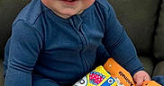 Colter joined the competition — help win amazing prizes! baby, child, blue_onesie, smile, happy, couch, fabric_book, colorful, toy, sitting, indoor, face, hands, cheeks, cute, infant, play, clothing, person, portrait