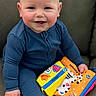 baby, child, blue_onesie, smile, happy, couch, fabric_book, colorful, toy, sitting, indoor, face, hands, cheeks, cute, infant, play, clothing, person, portrait