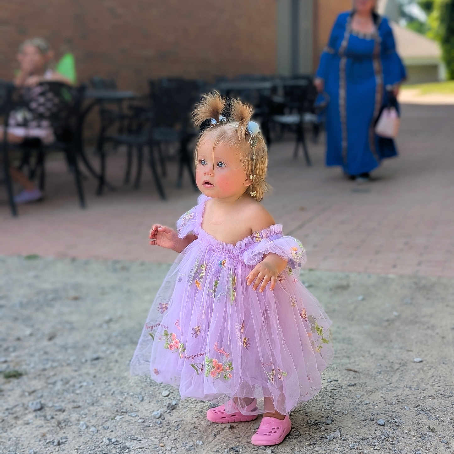 Ridlee Renee is registered to the contest to win money with this photo: adult, blurred_background, candid, chairs, child, curious_expression, daytime, dress, gravel, hair_accessories, lavender, outdoor, person, pigtails, pink_shoes, portrait, sidewalk, sunny, table, toddler