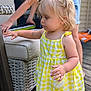 toddler, child, yellow_dress, gingham_pattern, lemon_patch, wicker_chair, outdoor, wooden_deck, person, keyboard, blonde_hair, pigtails, curious, exploration, summer, casual_clothing, daylight, playing_music, hand, portrait