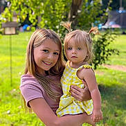 Ridlee Renee joined the competition — help win amazing prizes! child, toddler, sibling, smiling, outdoor, greenery, dress, pigtails, grass, sunlight, happy, portrait, nature, casual_clothing, holding, family, blonde_hair, summer, playground, cute