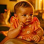 animal, baby, background, cat, child, close_up, cozy, curly_hair, cute, expression, flower_pattern, hand, indoors, infant, orange_dress, pet, portrait, skin, soft_focus, warm_light