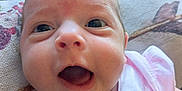 Rosalina is registered to the contest to win money with this photo: baby, infant, face, close_up, pink_clothing, expression, couch, pillow, happy, mouth_open, eyes, skin, head, newborn, person, indoors, portrait, cute, child, smiling