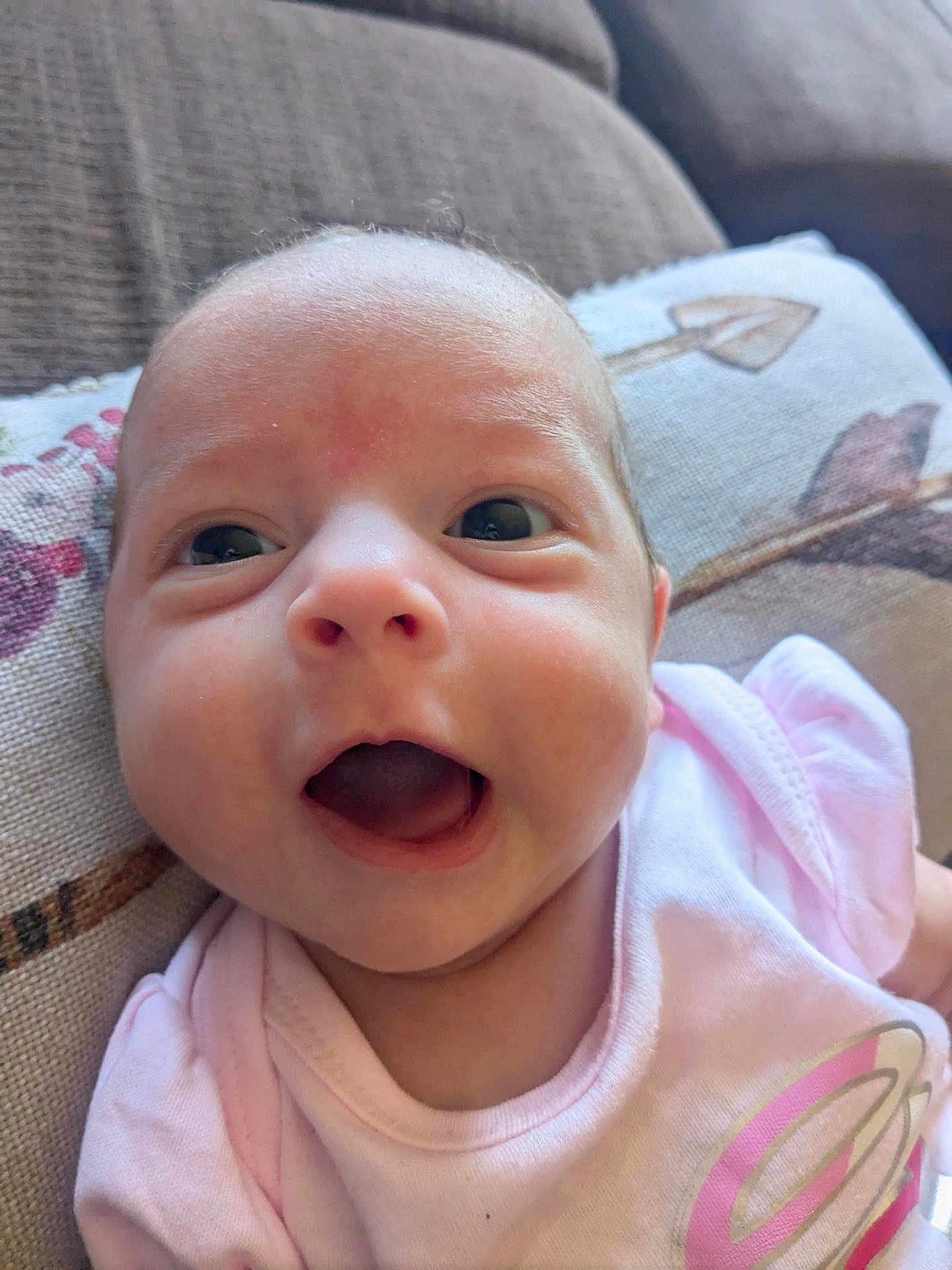 Rosalina is registered to the contest to win money with this photo: baby, infant, face, close_up, pink_clothing, expression, couch, pillow, happy, mouth_open, eyes, skin, head, newborn, person, indoors, portrait, cute, child, smiling