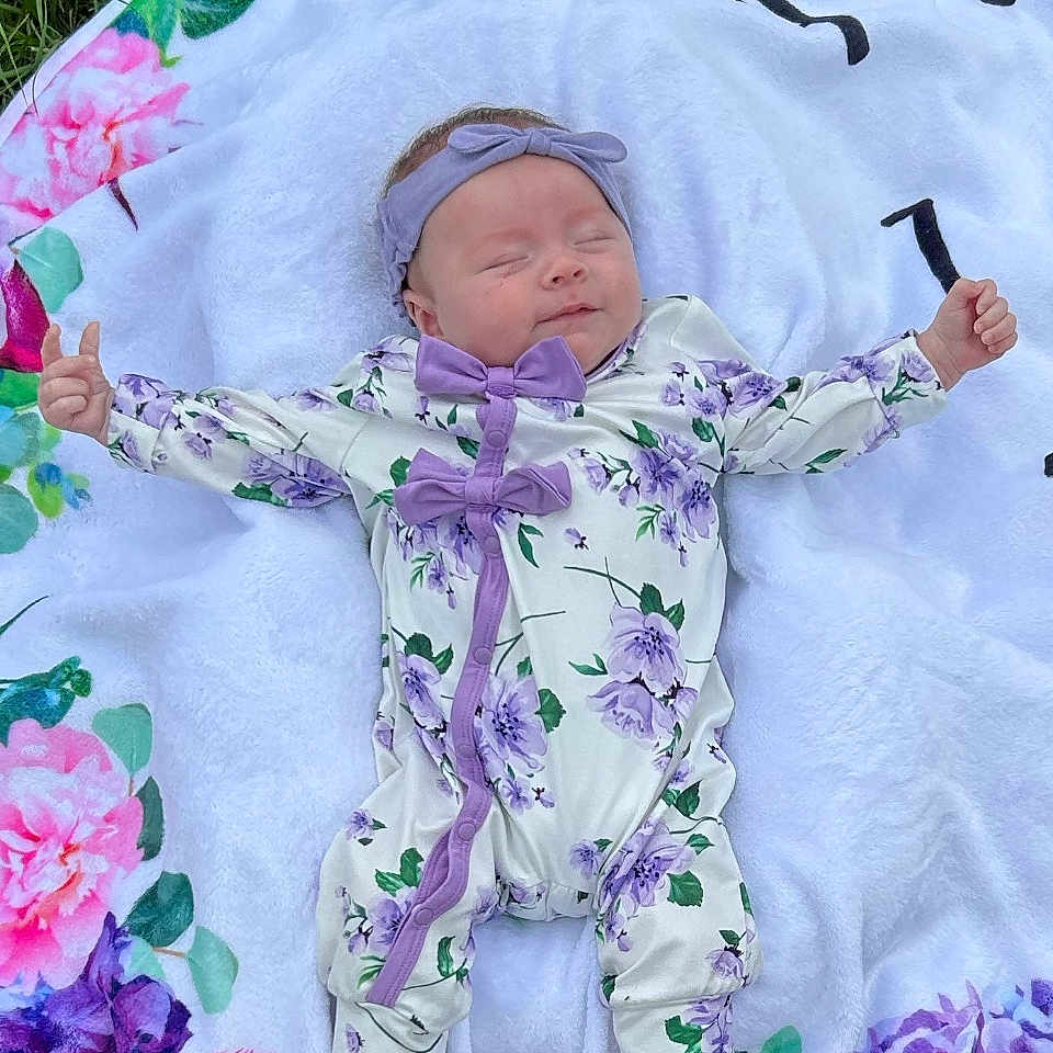 Cyndianna is registered to the contest to win money with this photo: baby, blanket, colorful, cute, floral, flower_pattern, grass, headband, infant, lying_down, nature, newborn, onesie, outdoor, peaceful, person, portrait, purple_bows, sleeping, soft_texture