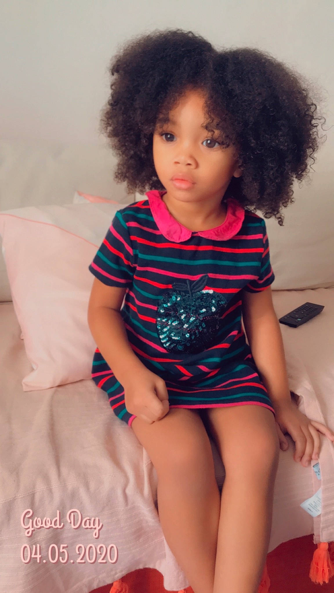 Amayah participe au concours pour gagner de l'argent avec cette photo : afro, black_hair, cheek, child, child_model, clothing, hair, hairstyle, human_leg, joint, leg, lip, long_hair, person, pink, shoulder, sitting, skin, t_shirt, thigh