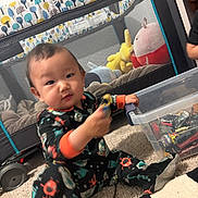 Andy is registered to the contest to win money with this photo: toddler, child, toy_car, pajamas, playpen, carpet, plastic_box, toys, indoor, person, baby, floor, plush_toy, stuffed_animal, hand, clothing, sitting, playing, room, vehicle