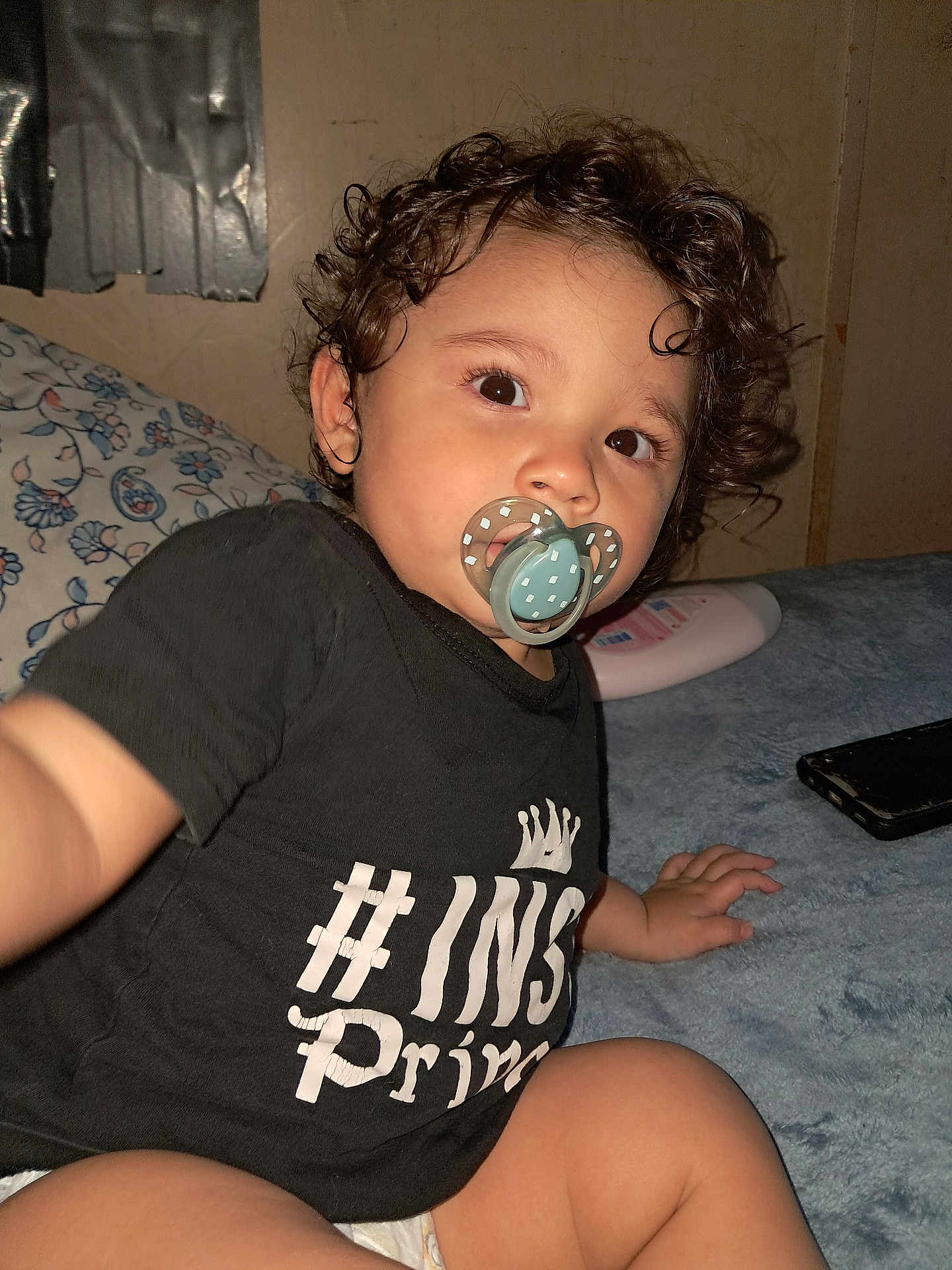 Alexis is registered to the contest to win money with this photo: toddler, child, curly_hair, pacifier, black_shirt, indoor, bed, pillow, baby_lotion, hand, face, cute, infant, person, young_child, casual, expression, closeup, skin, sitting