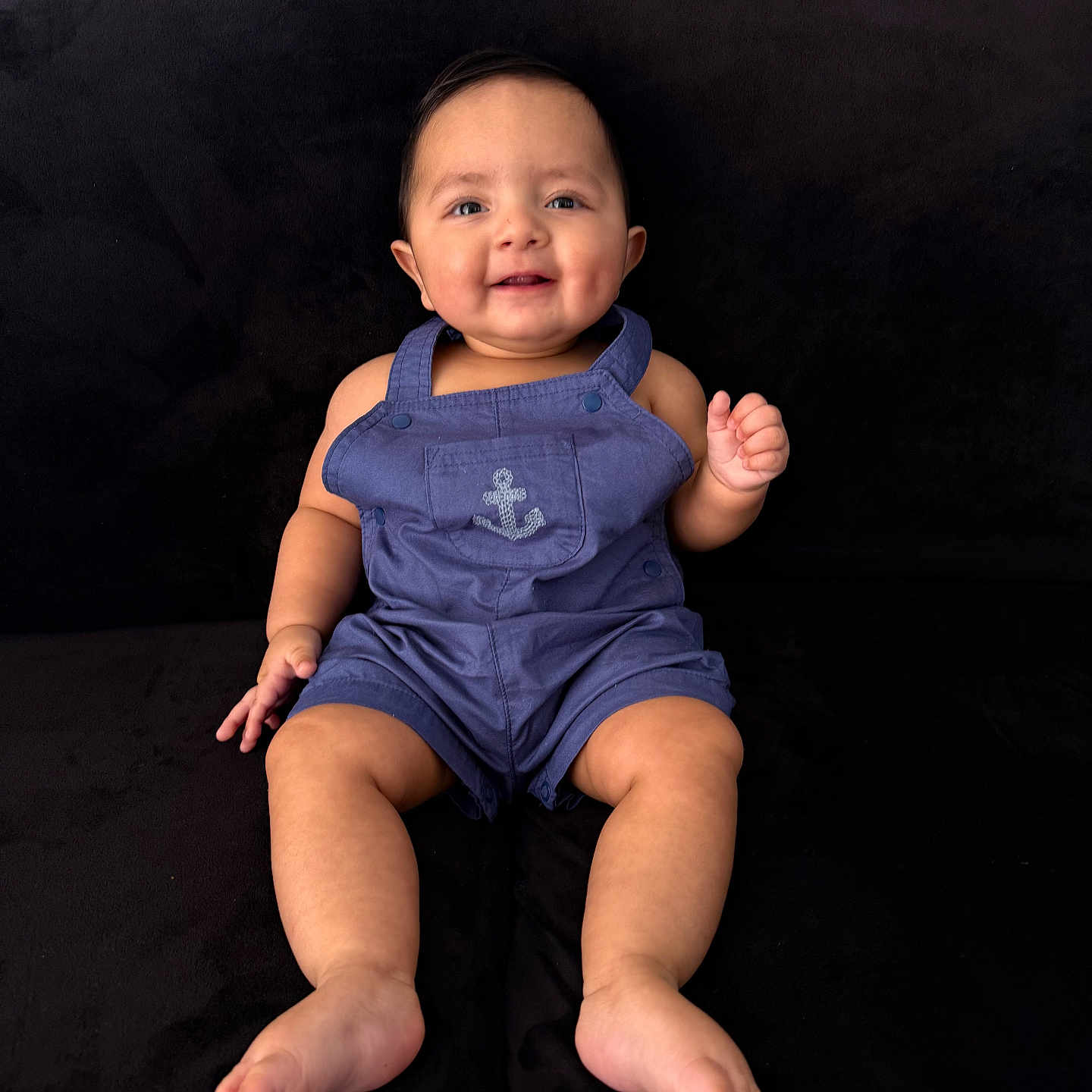 Hayes joined the competition — help win amazing prizes! baby, child, smiling, sitting, romper, blue_clothing, anchor_emblem, barefoot, chubby_cheeks, happy, face, portrait, indoor, couch, black_background, cute, person, infant, young_child, casual