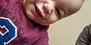 Noah joined the competition — help win amazing prizes! baby, child, smiling, teeth, closeup, portrait, indoor, tshirt, maroon_shirt, arm, adult_arm, candid, playful, curly_hair, forehead, wall, hardwood_floor, person, happy, squinting