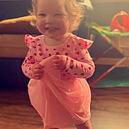 Lorelei is registered to the contest to win money with this photo: toddler, child, indoor, smiling, dress, bow, pink, hearts, socks, wooden_floor, window, sunlight, play_area, happy, person, curly_hair, cute, standing, fabric, home