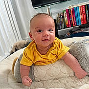 Carson joined the competition — help win amazing prizes! baby, infant, yellow_shirt, smile, face, plush, cushion, indoor, bookshelf, books, television, soft_toys, blanket, person, home, child, curious, happy, floor, furniture